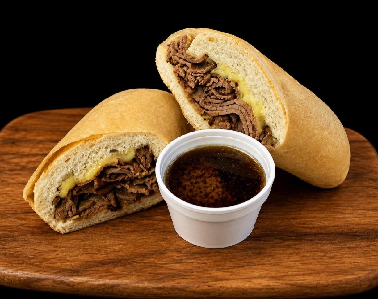 Classic French Dip sandwich cut in half, piled with sliced beef and melted provolone, with a cup of au jus